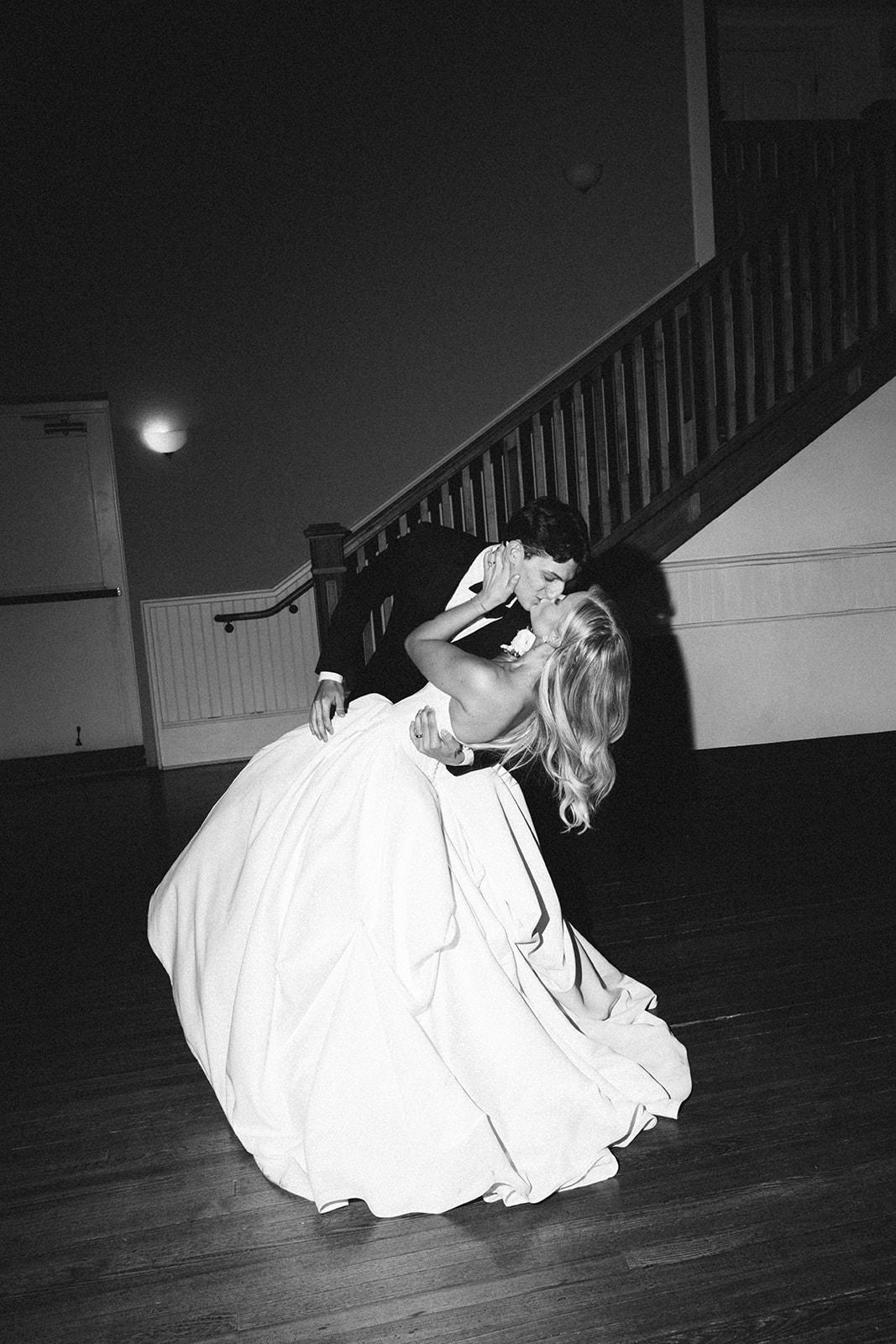 A bride and groom share a kiss while dancing in a dimly lit room, with stairs in the background at Stanly Hall Ballroom