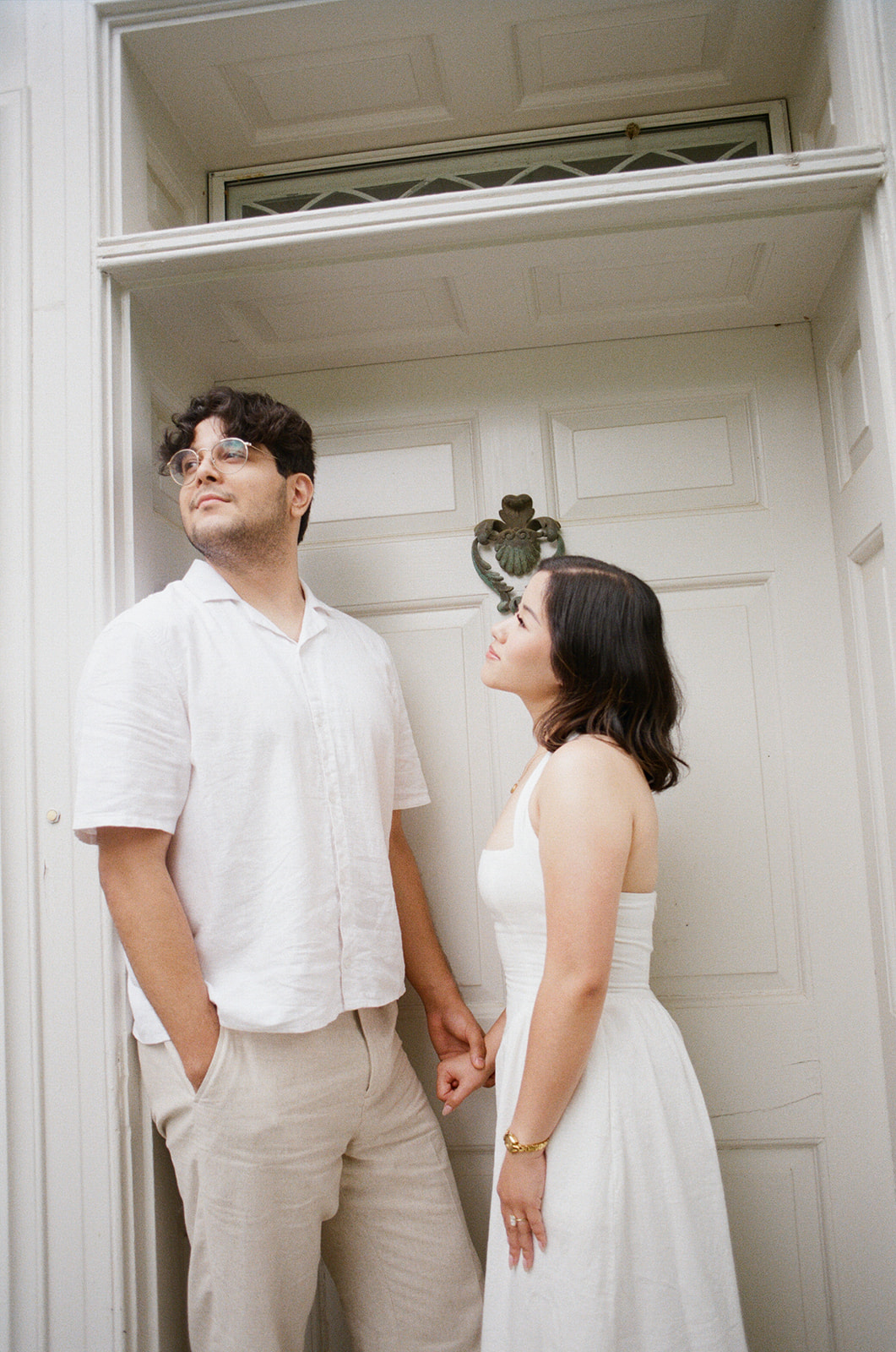 A couple dressed in white stands close together outdoors, looking into each other's eyes with greenery and flowers in the background. |What to Wear for Engagement Photos