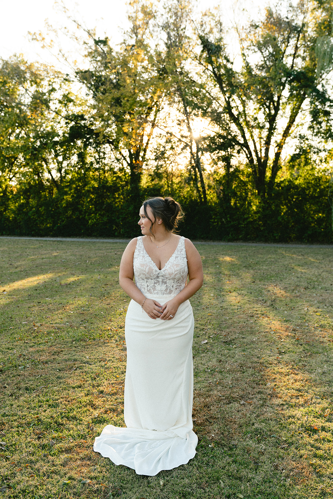 A bride and groom stand together outdoors on a grassy field, holding hands and looking at the camera, with trees in the background. | How to Choose a Wedding Photographer