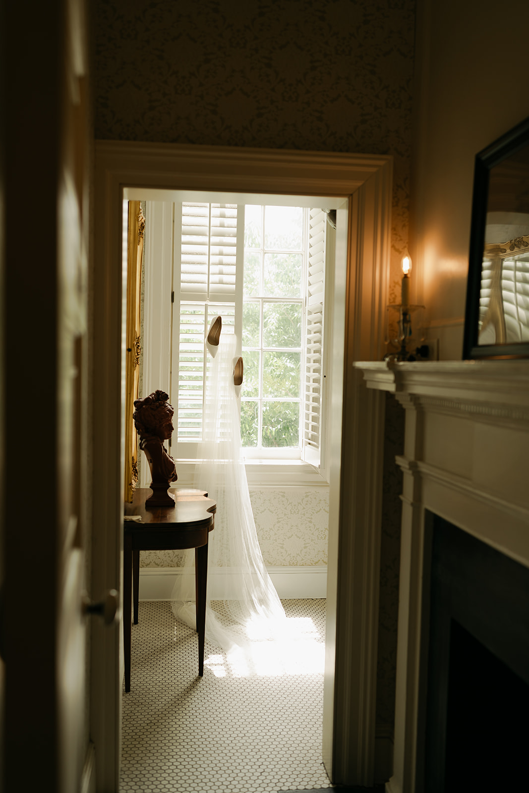 A bridal veil draped over a mauve chair with a bouquet of white flowers and a pair of white high-heeled shoes placed on the seat.