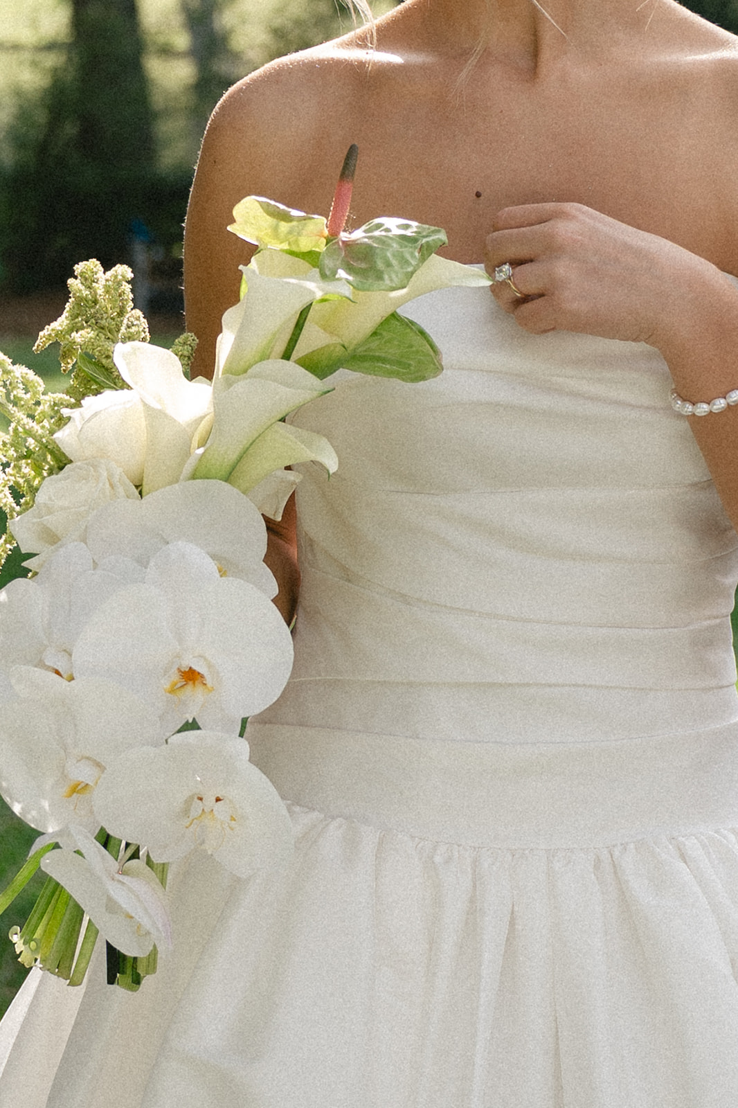 A bride in a white wedding dress stands outdoors on grass, holding a bouquet, with two floral arrangements on white pedestals behind her for a Charleston wedding