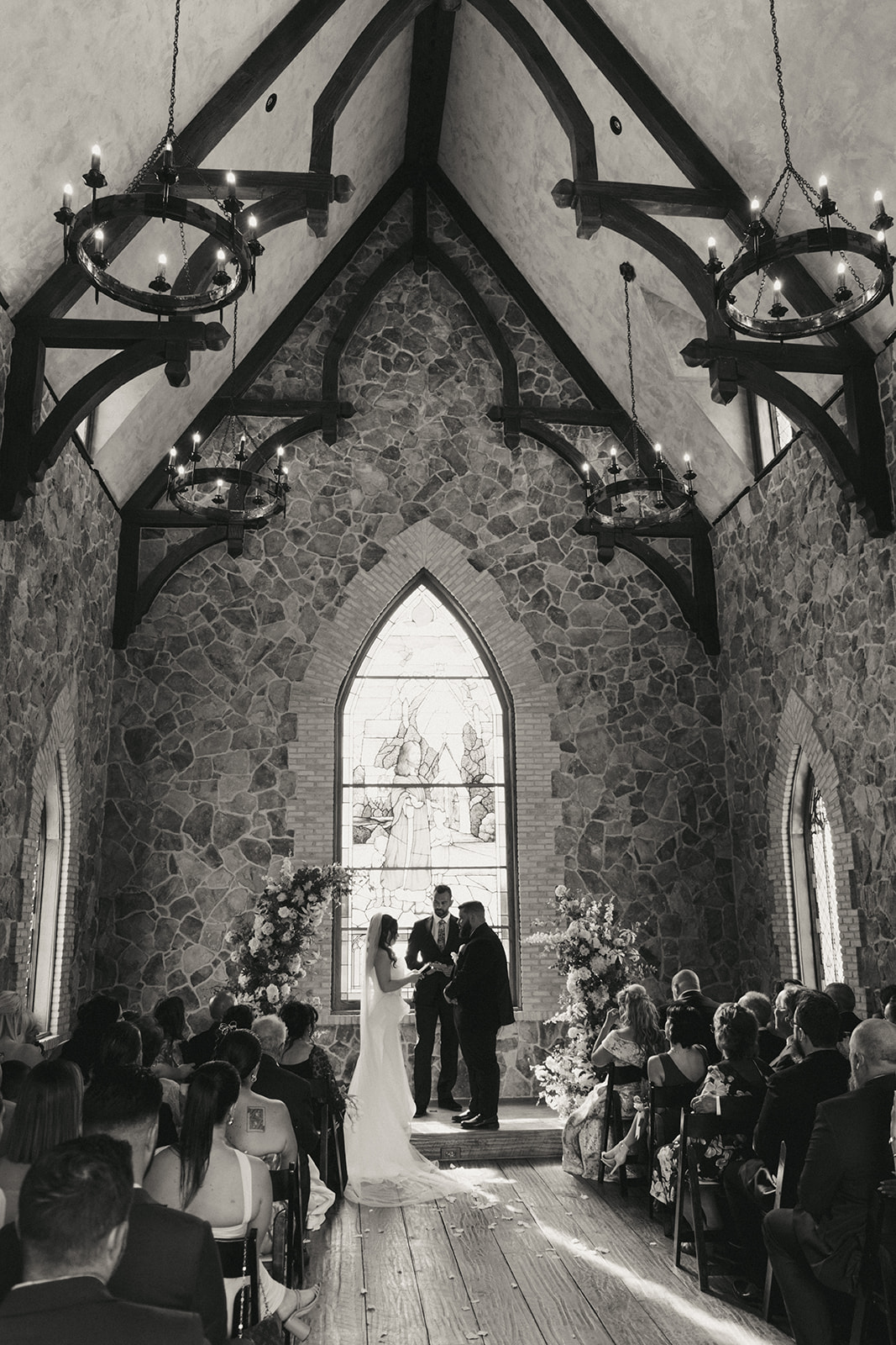 A bride and groom stand at the altar with an officiant in a stone chapel, surrounded by seated guests at the little chapel at haven ridge a wedding venue in North Carolina 