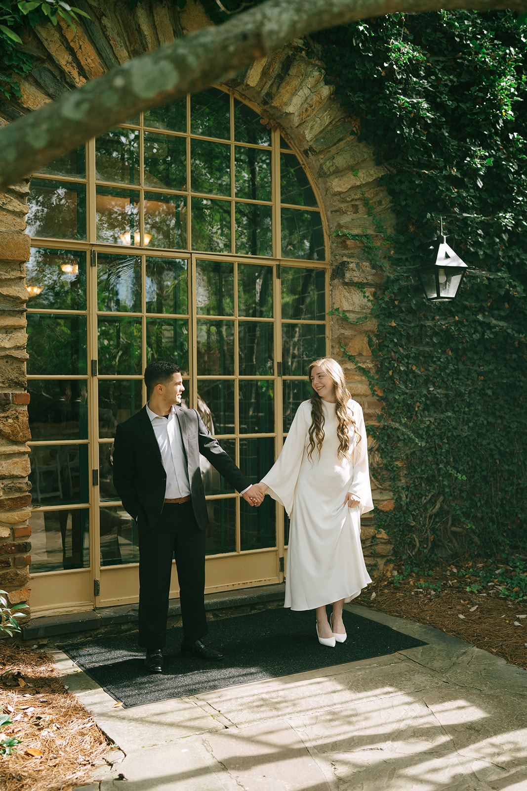 Two people stand together on a lawn, seen through a window with metal bars, with trees and greenery in the background.