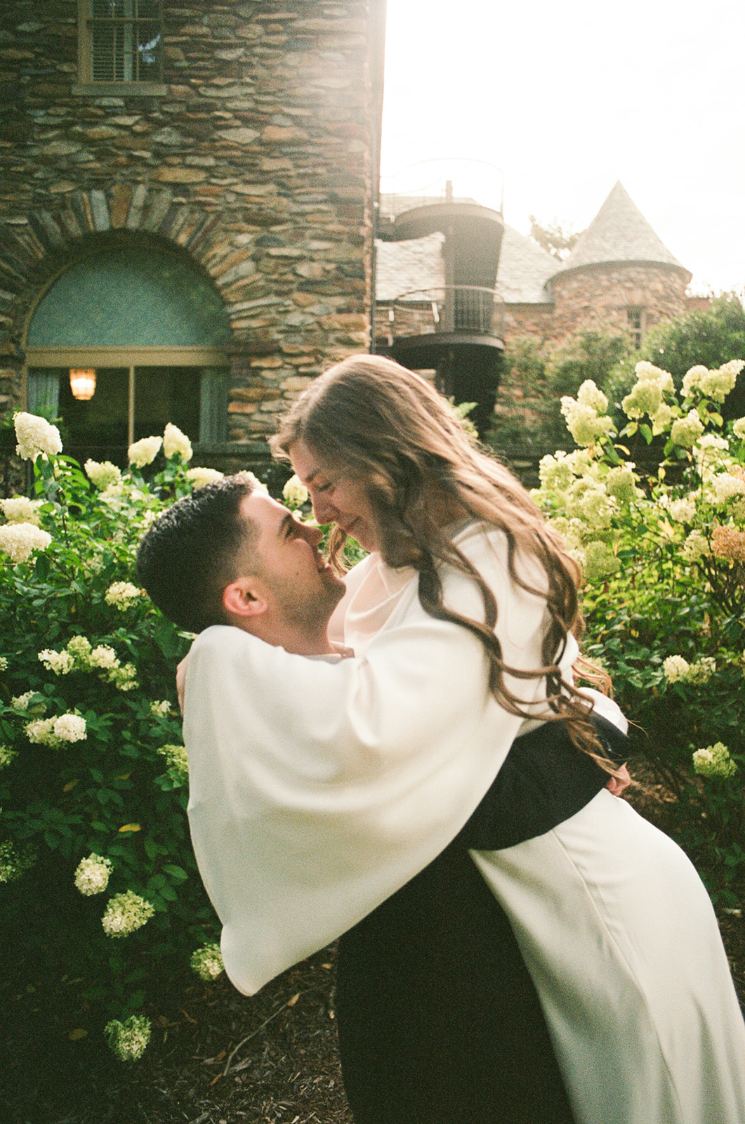 A person in a suit and a person in a white dress while standing in a garden with blooming white flowers at Graylyn Estate a wedding venue in North Carolina