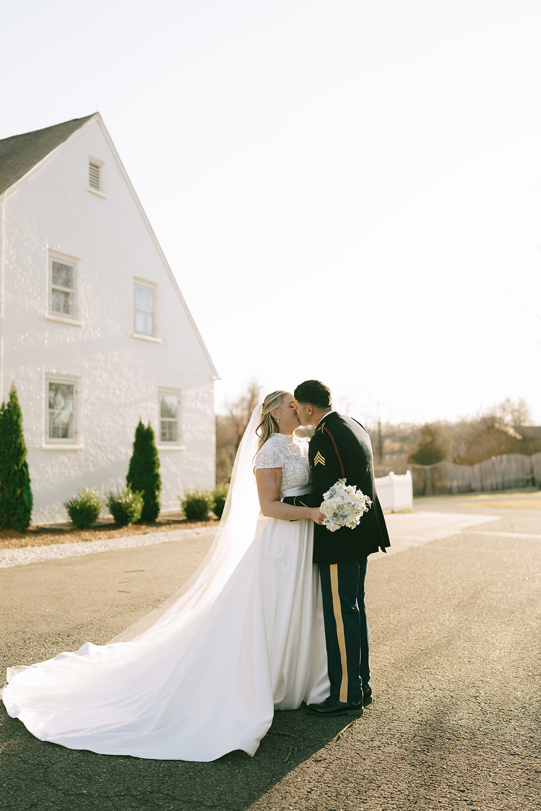 A bride and groom in wedding attire share a kiss outdoors on a sunny day at The Vintage Oak Estate a wedding venue in North Carolina 