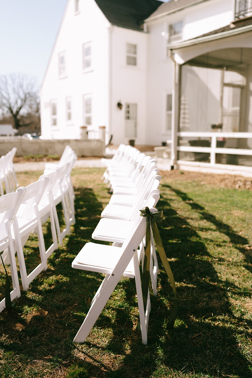 Rows of white folding chairs set up outdoors on grass, facing a white house for a wedding at the The Vintage Oak Estate