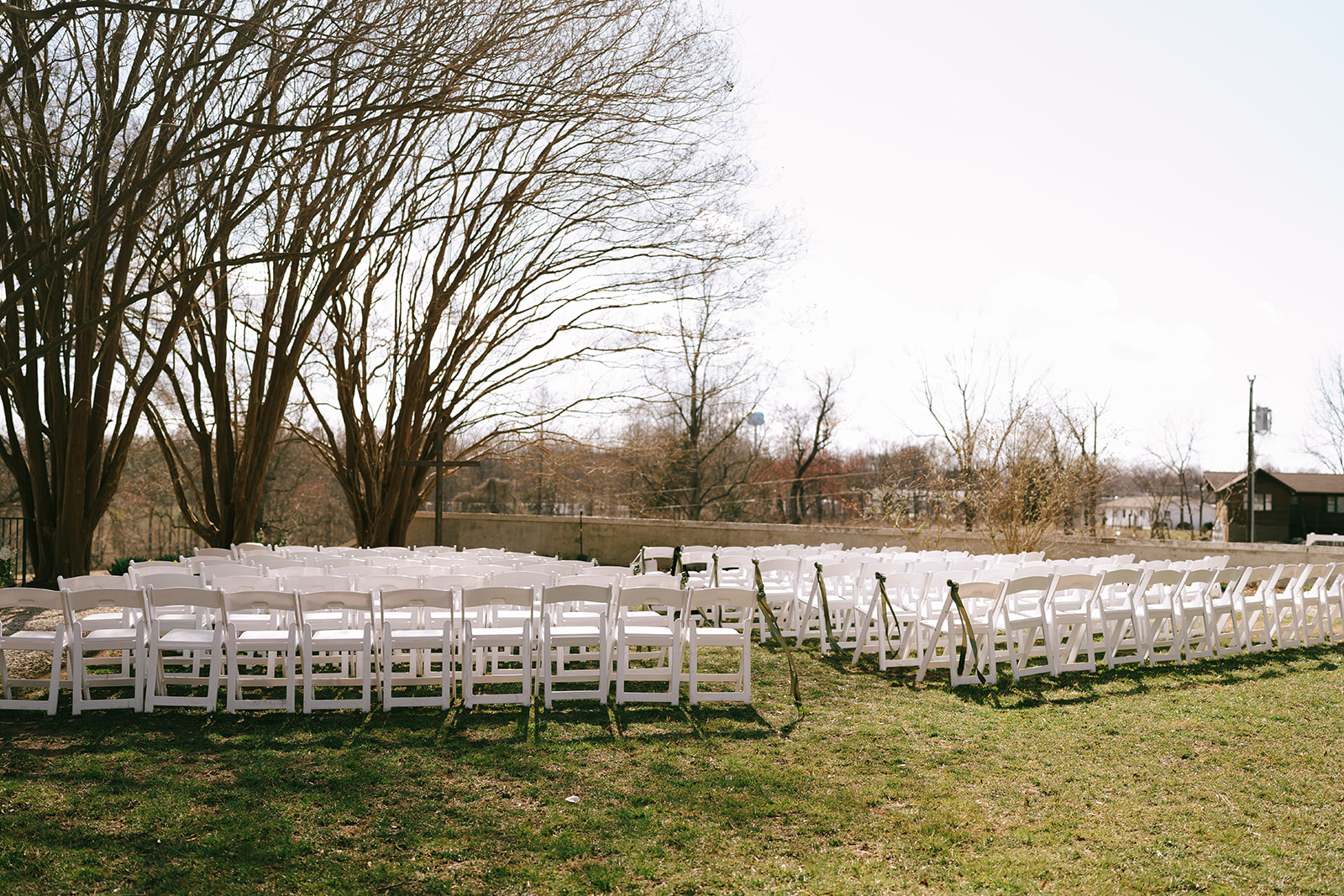 Rows of white folding chairs set up outdoors on grass, facing a white house for a wedding at the The Vintage Oak Estate