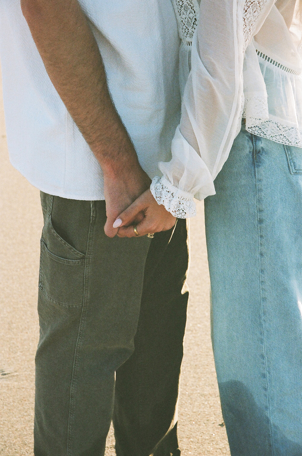 Two people standing side by side and holding hands, one wearing a white shirt and dark pants, the other in a white blouse and light blue jeans.
