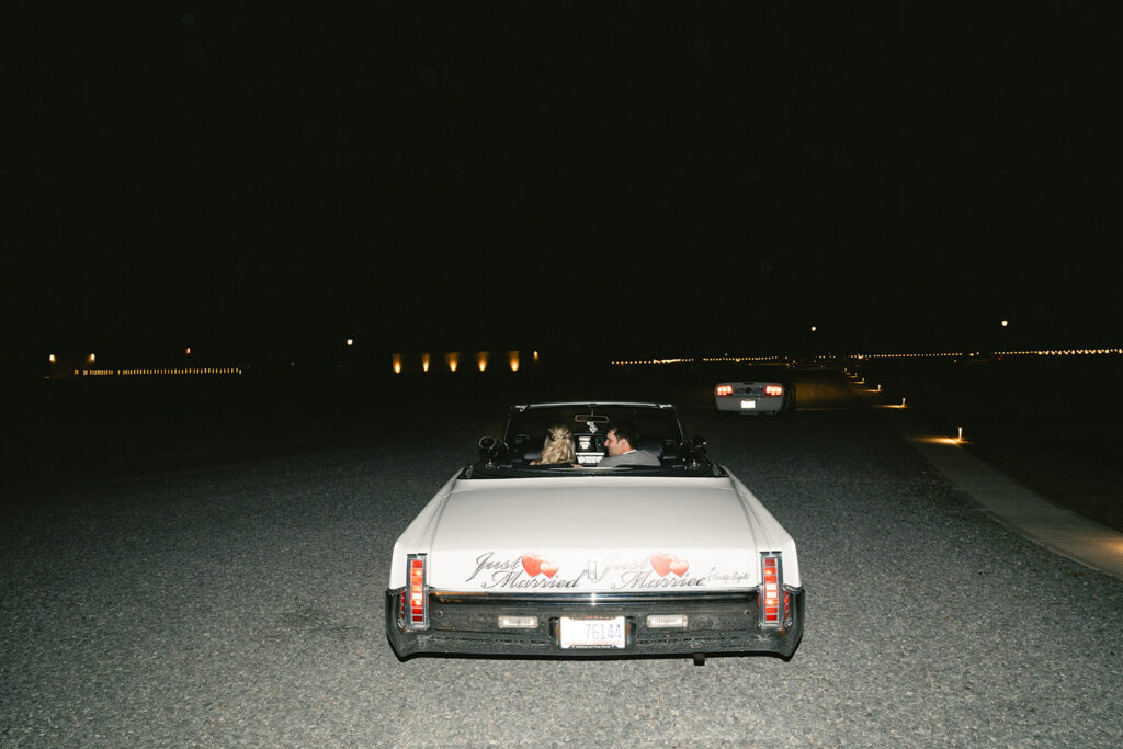 A white convertible drives down a dark road at night with two people inside; another car is visible ahead in the distance taken by a North Carolina wedding photographer